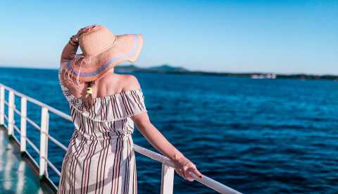 Rear view of a woman wearing a sun hat on ship deck looking at horizon over sea