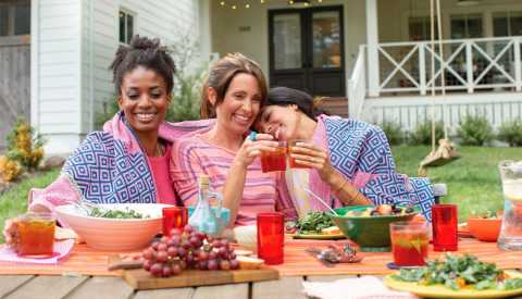 three women sitting outside at a table with salads and grapes