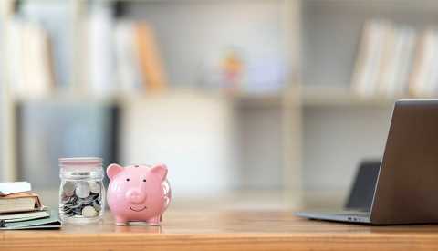 Smiley piggy bank next to a jar of coins on wooden table