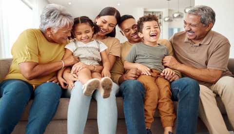 four adults and two children sitting together on a couch and laughing