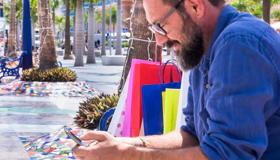 Man on bench with shopping bags checks phone 