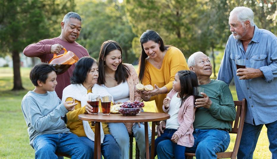 A large multi-generation and extended family spending time together in the back yard, eating snacks and drinking refreshments. The group includes three grandchildren, three grandparents and an interracial Asian and Caucasian couple.
