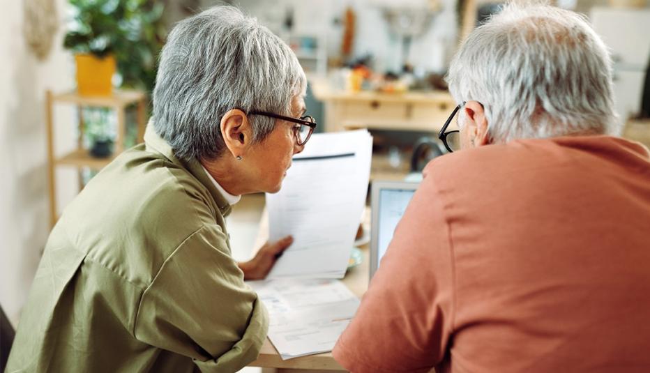 Two older adults looking at a laptop and paperwork at the dinning room table.