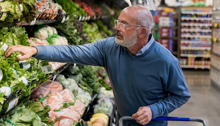 Older man reaching for vegetables in the grocery store.
