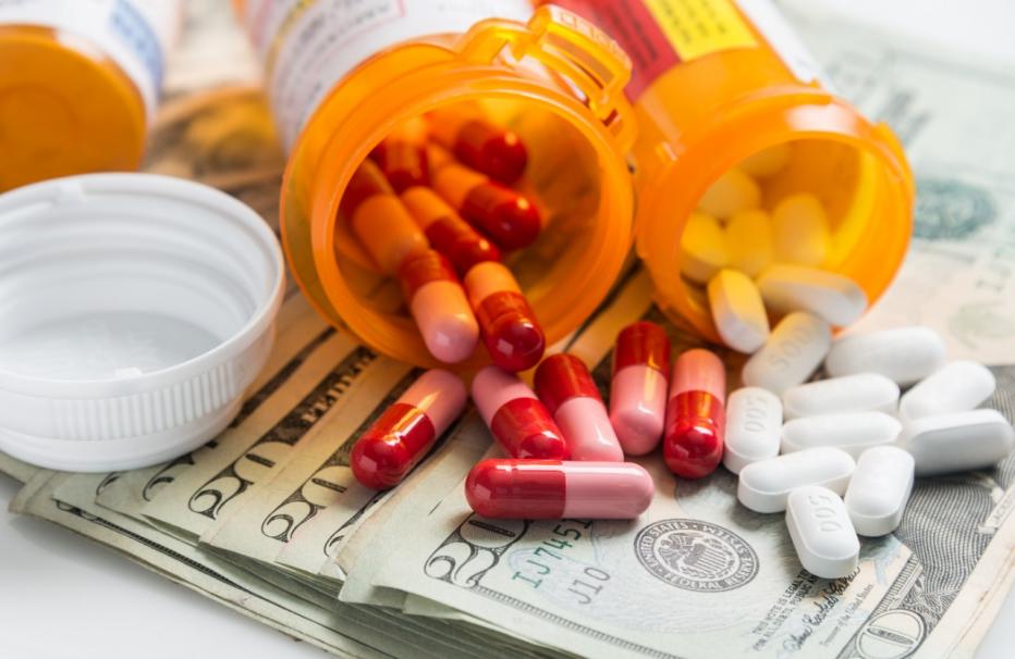 Pile of 20 dollar bills with prescription bottles on top spilling pills on the 20 dollar bills.