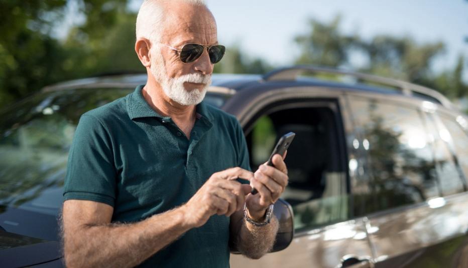 Senior man leaning on his car and texting a message.