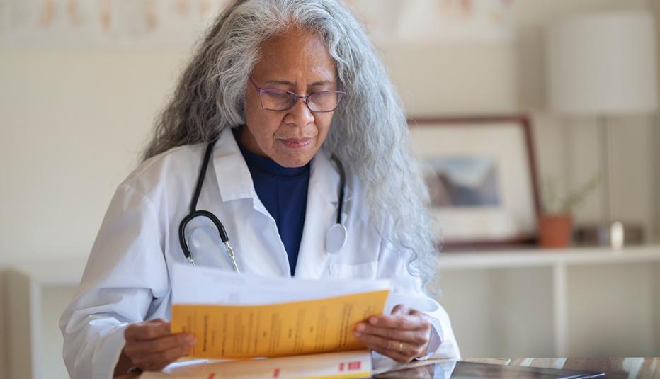 A mature adult female doctor of Pacific Islander and Asian descent reviews a patient's file while working in her office.