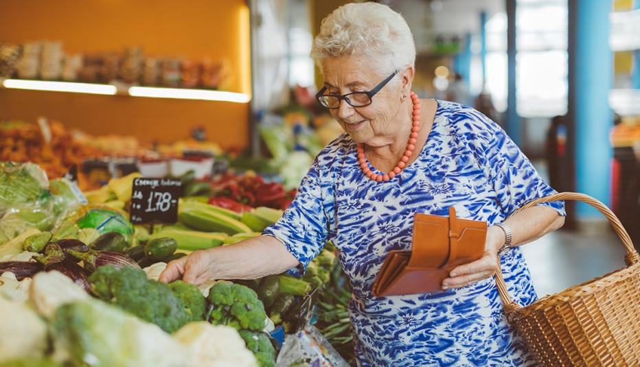 Senior woman with grey hair and glasses shopping for vegetables in a market.