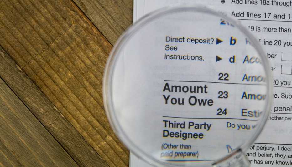 IRS tax Form on wooden surface with the "amount you owe" section under a magnifying glass