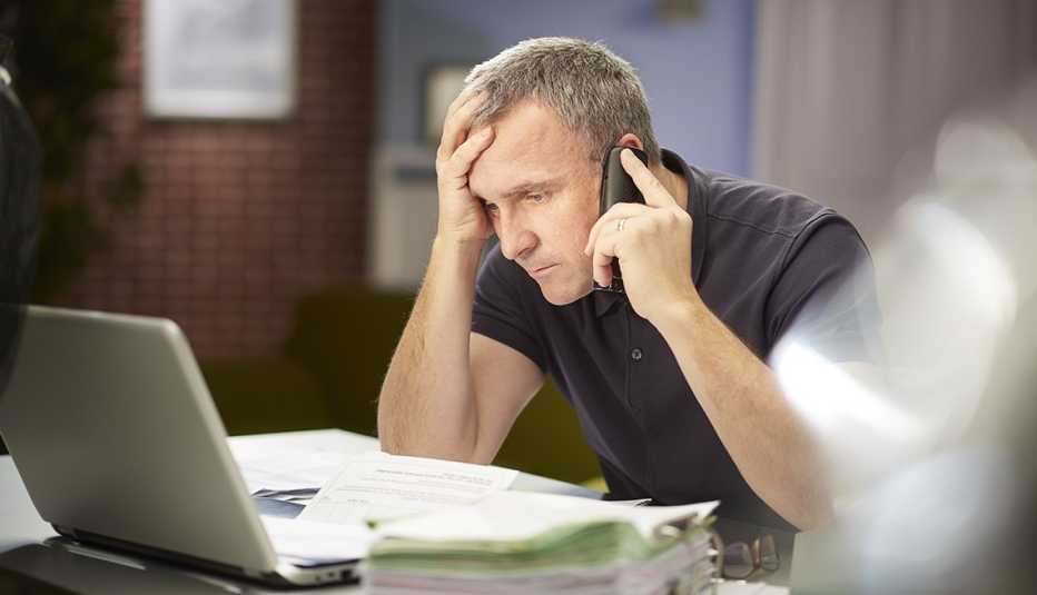 man looking at laptop screen while holding his phone and waiting for a customer service representative 