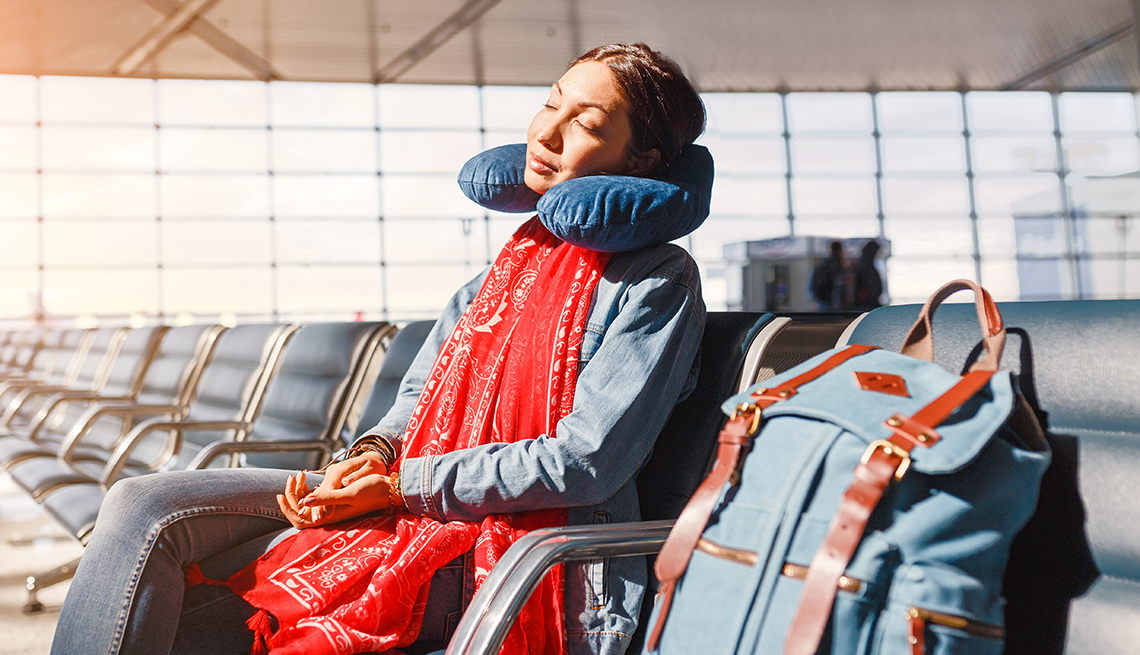 woman at airport resting in the boarding wait area with a neck pillow and her backpack