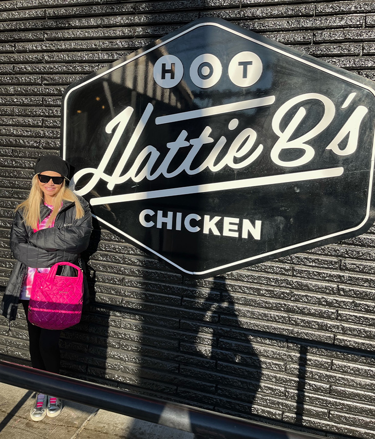 kristin chenoweth outside, next to sign that says hattie b's hot chicken