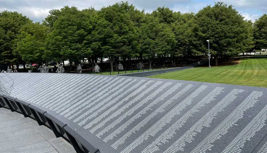 the korean war veterans memorial wall of remembrance with the older statues of soldiers under the trees in the background