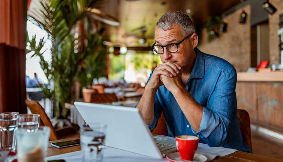 a concerned man sits with his hands folded looking at his laptop