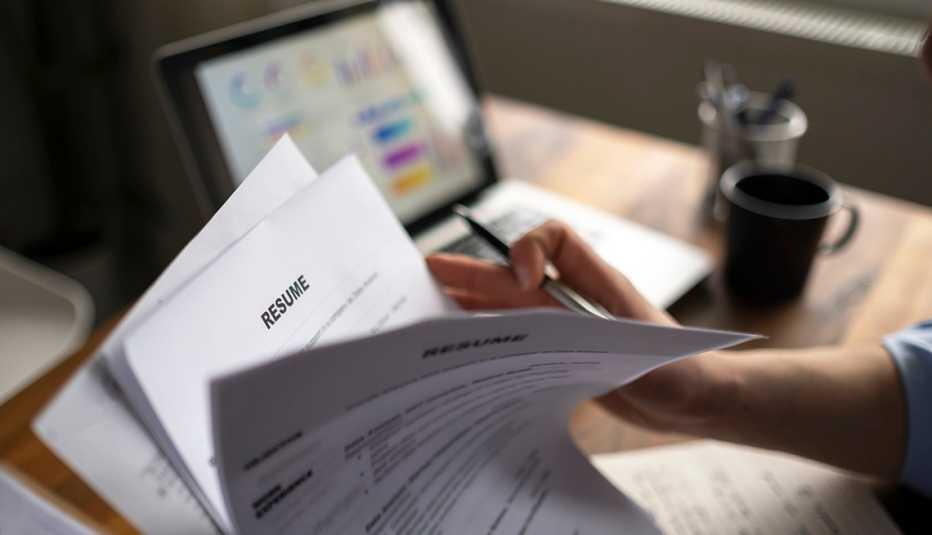 hand of a corporate recruiter shuffling through a pile of printed resumes with a laptop in the background on the desk