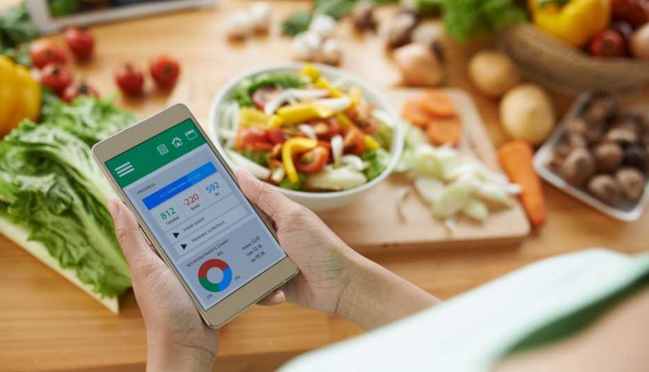 Mujer usa su teléfono mientras corta vegetales