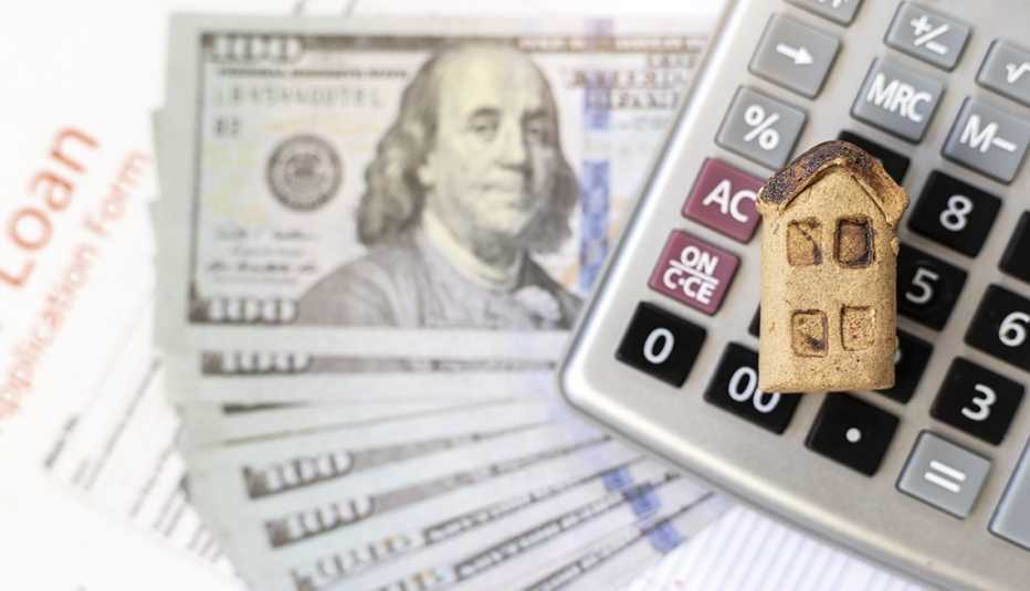 Casa en una miniatura sobre una calculadora, billetes de 100 dólares, y un formulario de préstamo. 