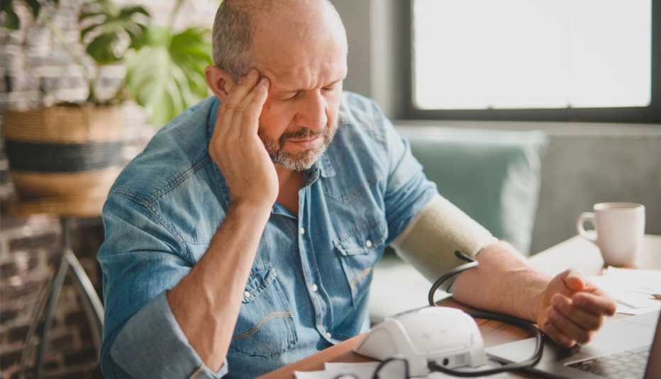 Hombre luce preocupado mientras ve sus facturas médicas y se toma la presión arterial