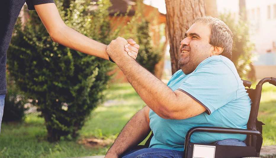 Hombre en una silla de ruedas sostiene la mano de otra persona.