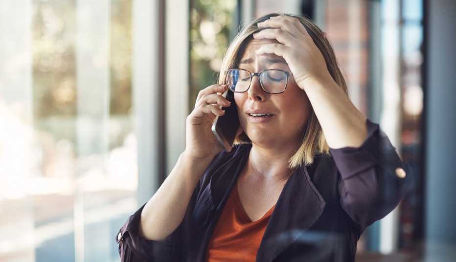 Mujer con expresión de preocupación con una mano en la cabeza y la otra sostiene el teléfono.