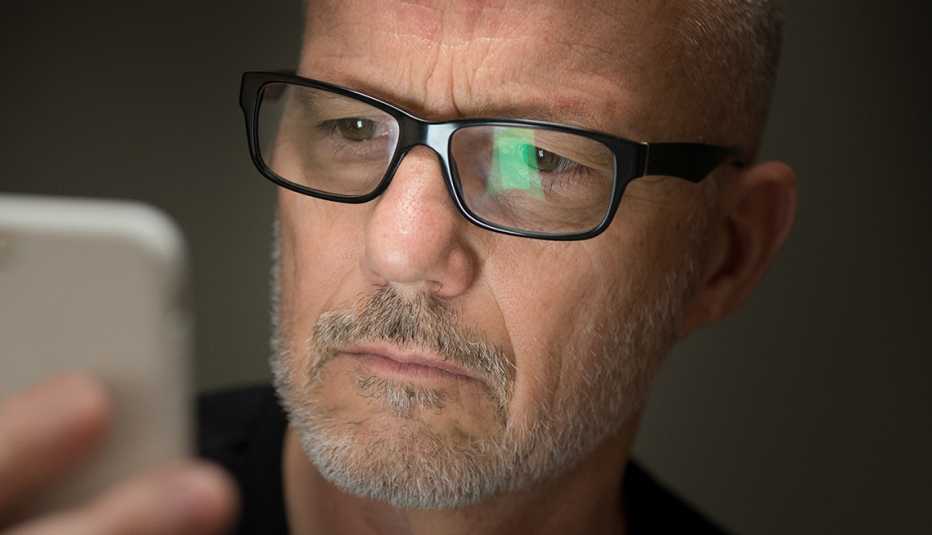 Hombre con lentes sosteniendo un teléfono móvil en su mano y mirando su pantalla.