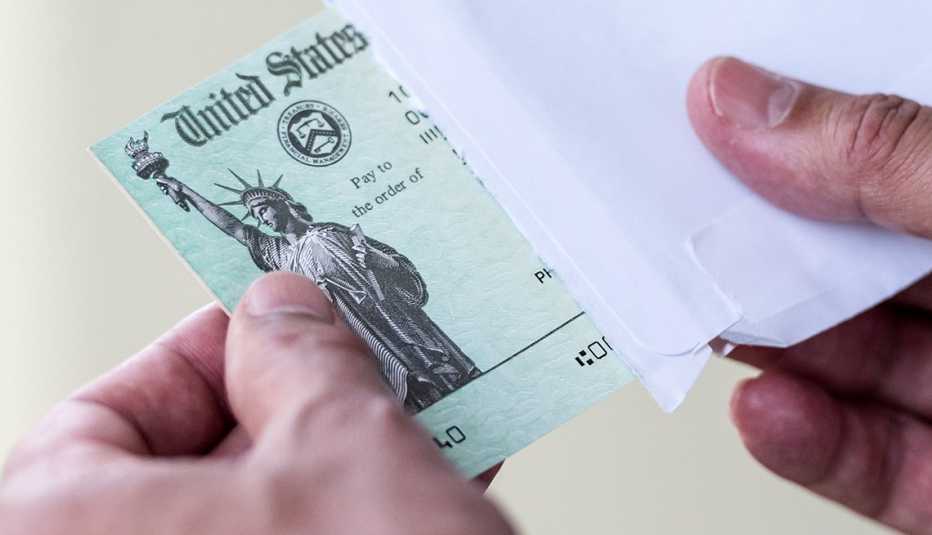 Manos sacando un cheque del tesoro de Estados Unidos de un sobre.