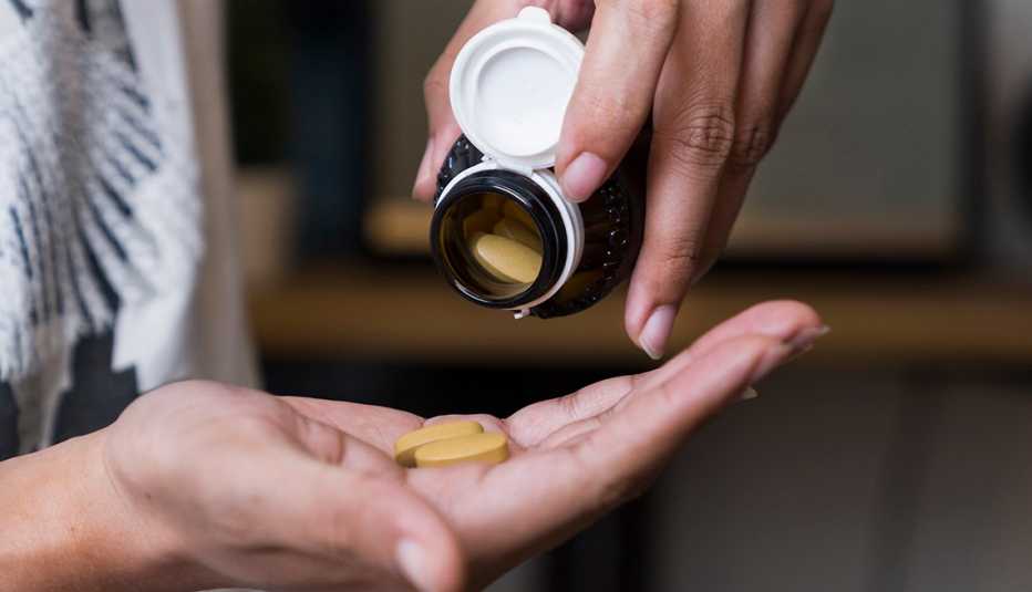 Mujer con un tarro de pastillas en una mano y algunas en la otra.