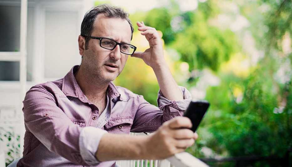 Hombre mirando un teléfono celular sentado en un balcón.