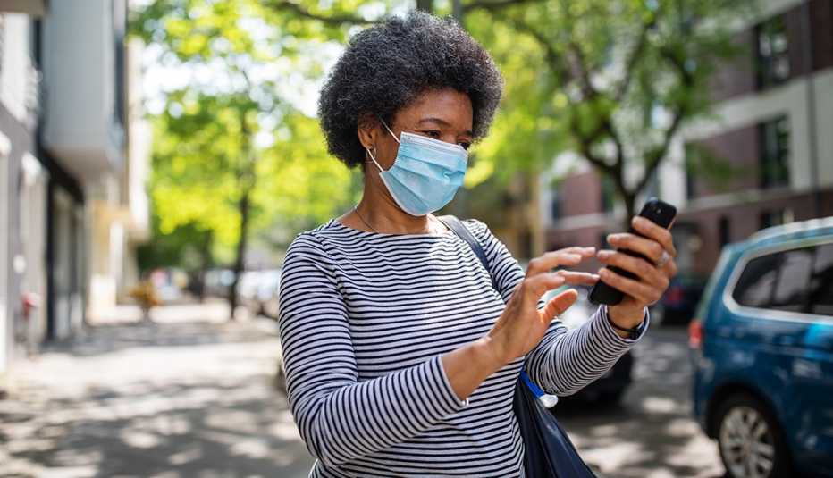 Mujer con una mascarilla en la calle y viendo su teléfono móvil.