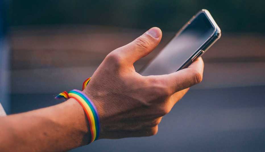 Mano sostiene un teléfono móvil con un bracelte con los colores del arco iris