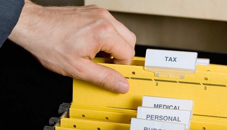Hombre saca carpeta etiquetada con la palabra impuestos de un archivo