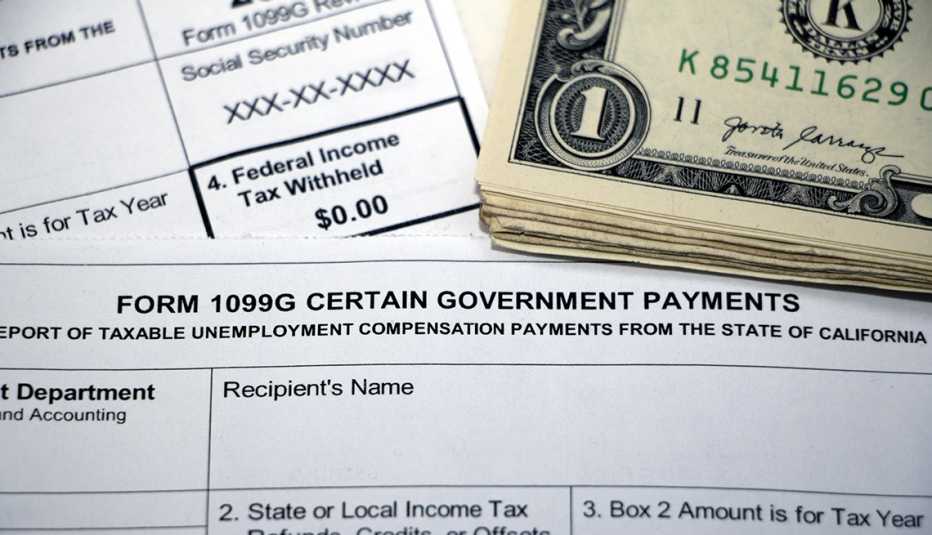 Formularios 1099G, y de impuestos federales debajo de un fajo de billetes de dólar.