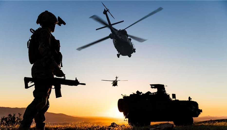 Soldado al atardecer y al fondo dos helicópteros y un carro de combate.