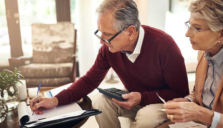 Pareja mayor haciendo cuentas en una calculadora y un cuaderno de notas.