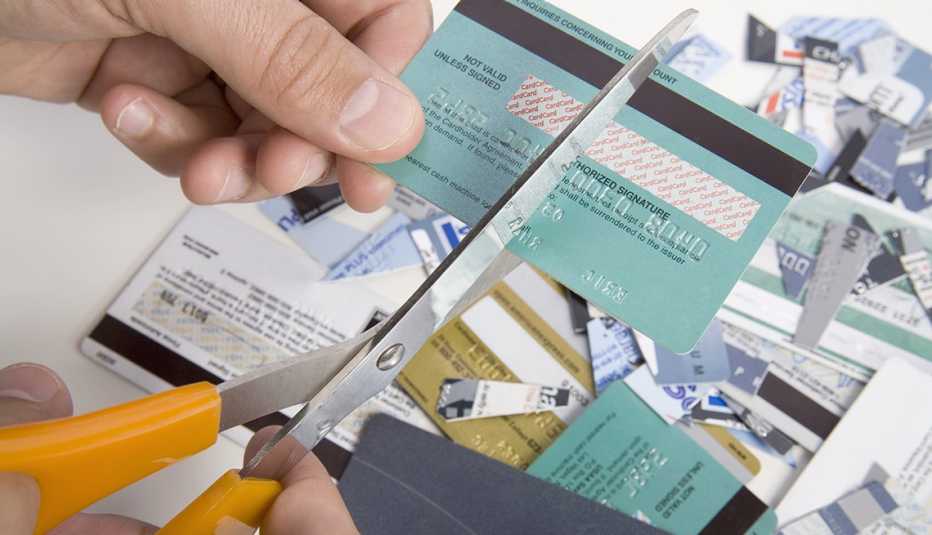 Manos de una personas usando unas tijeras para cortar varias tarjetas de crédito.