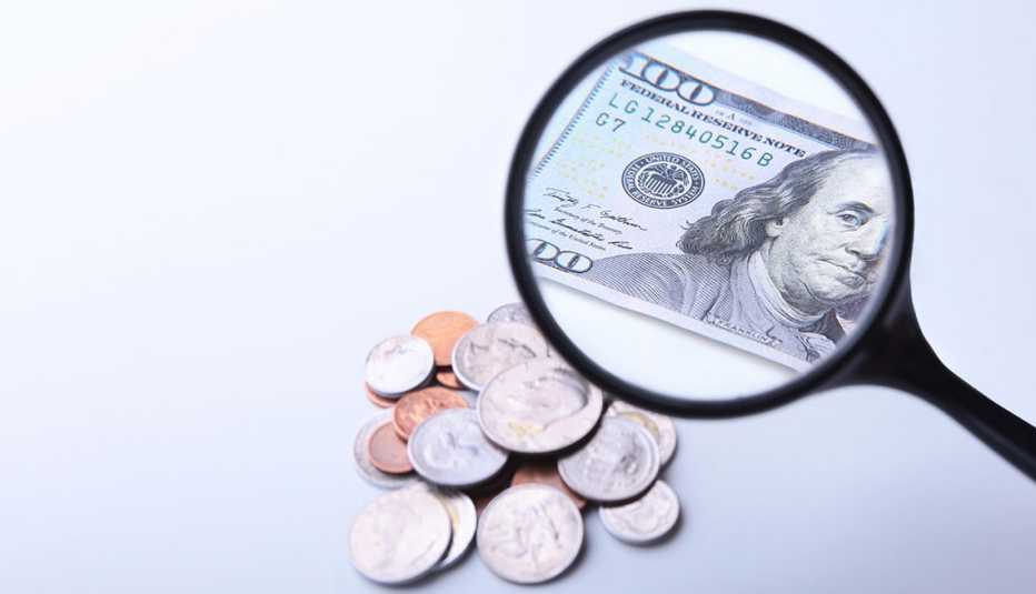 Monedas y un billete de 100 dólares visto a través de una lupa
