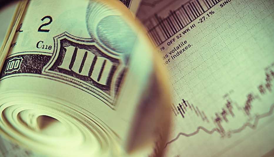 Rollo de billetes de 100 dólares sobre una gráfica del mercado de valores.