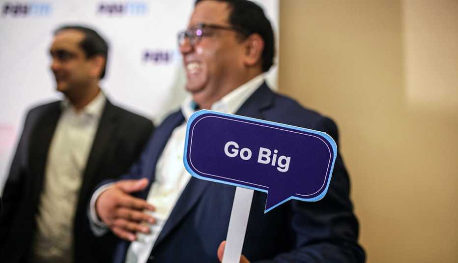 Inversionistas en una conferencia y uno de ellos sostiene un letrero que dice ve en grande