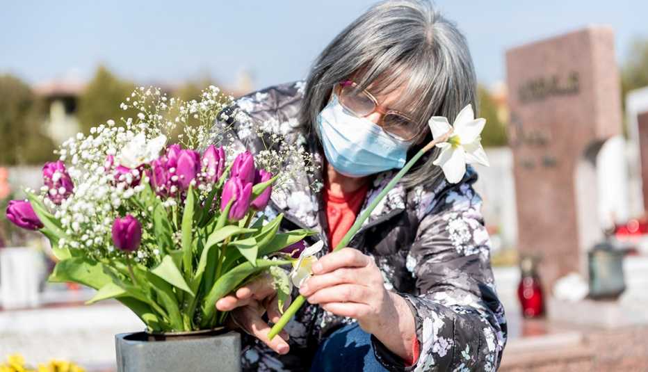 Mujer con tapabocas coloca flores en un cementerio