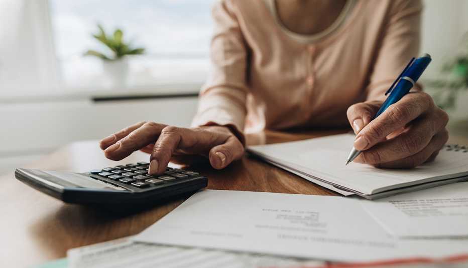 Manos de una mujer haciendo cuentas con una calculadora, papel y lápiz.