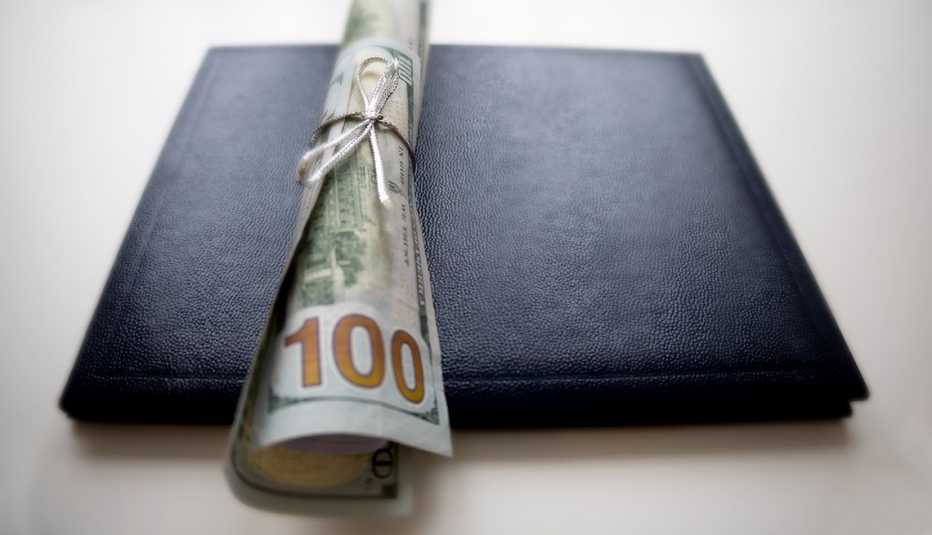 Un birrete de graduación con un billete de cien dólares enrollado encima.