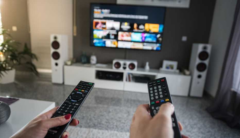 Mano de una mujer y un hombre que sostienen los controles de un televisor que muestra proveedores de servicios en línea