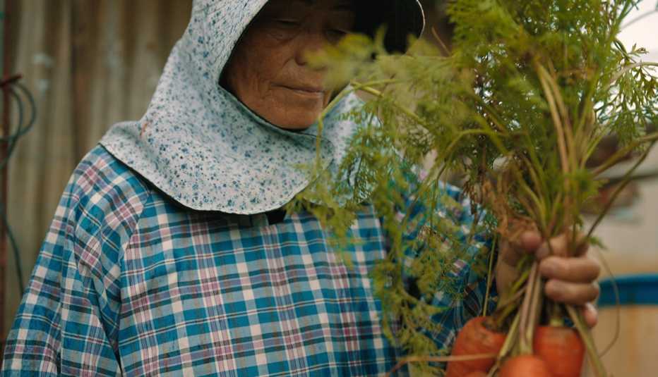 Una persona con zanahorias en sus manos en una escena de "Live to 100: Secrets of the Blue Zones".