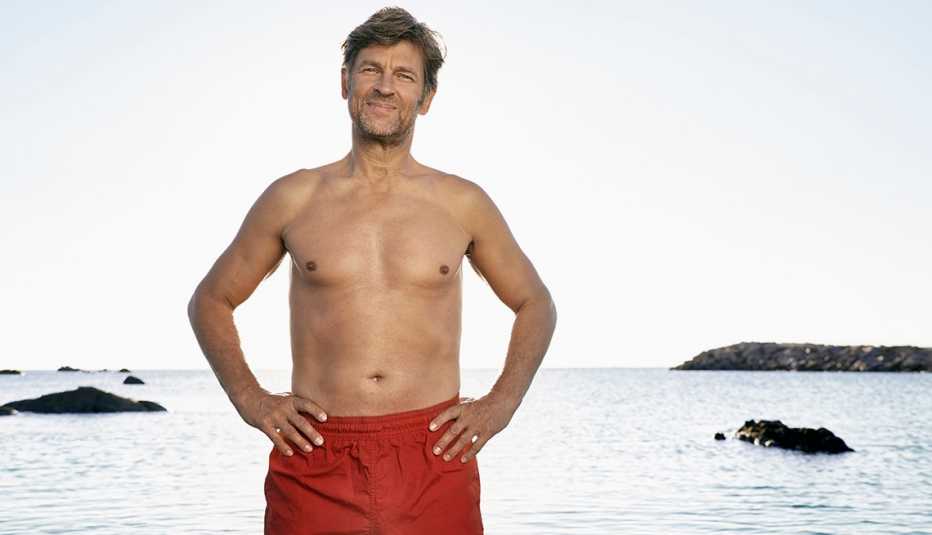 Un hombre usando una pantaloneta de baño con el mar al fondo.
