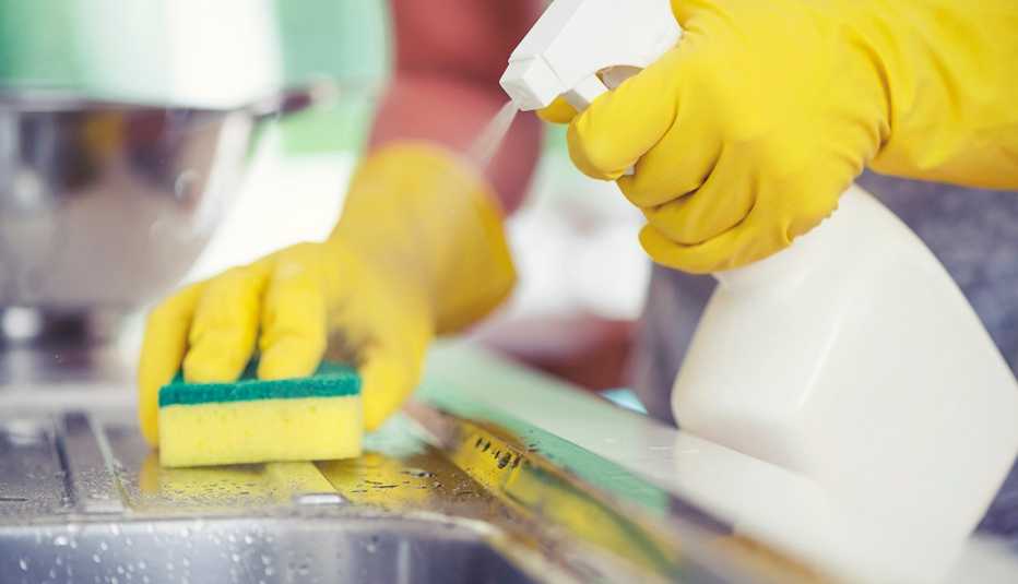 Persona limpia el fregadero de la cocina con una esponja y una botella de spray