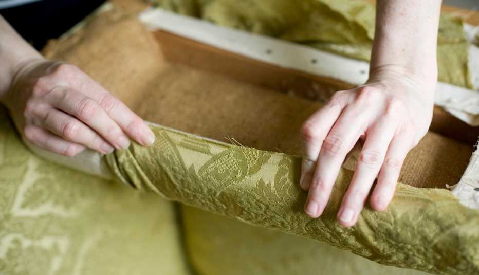 Manos tapizando una silla con tela verde