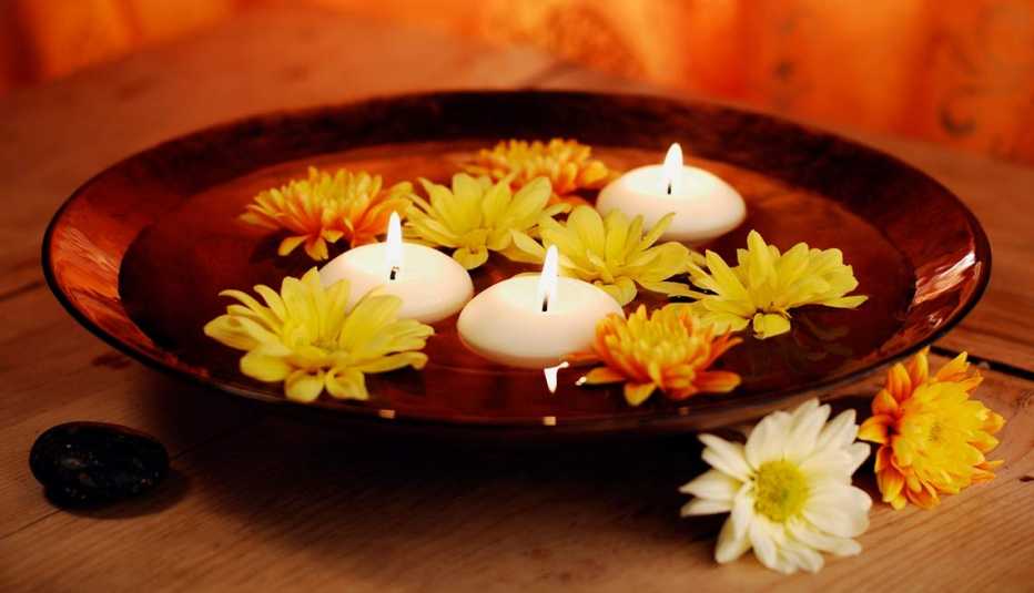 Flores y velas flotando en agua dentro de un recipiente de vidrio