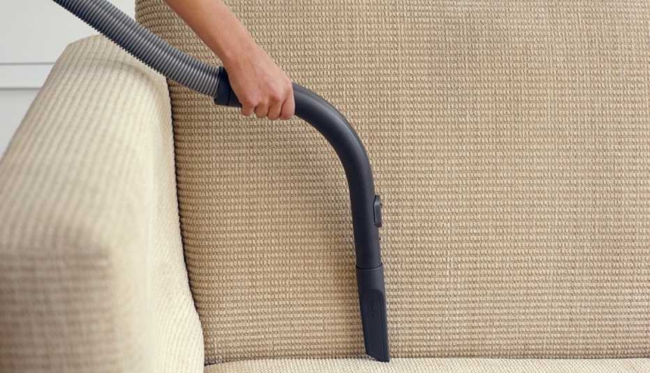 Una mano con una aspiradora limpiando un asiento