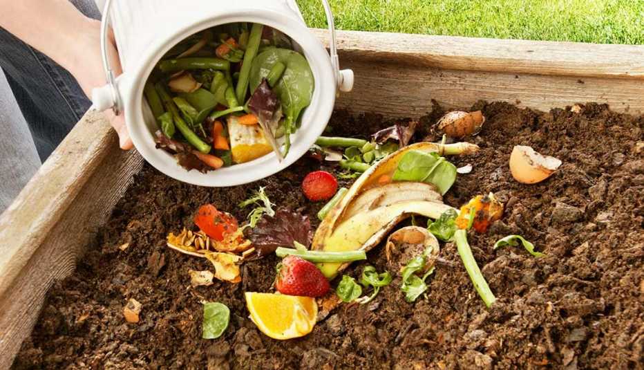 Una persona echando vegetales en un depósito de composta