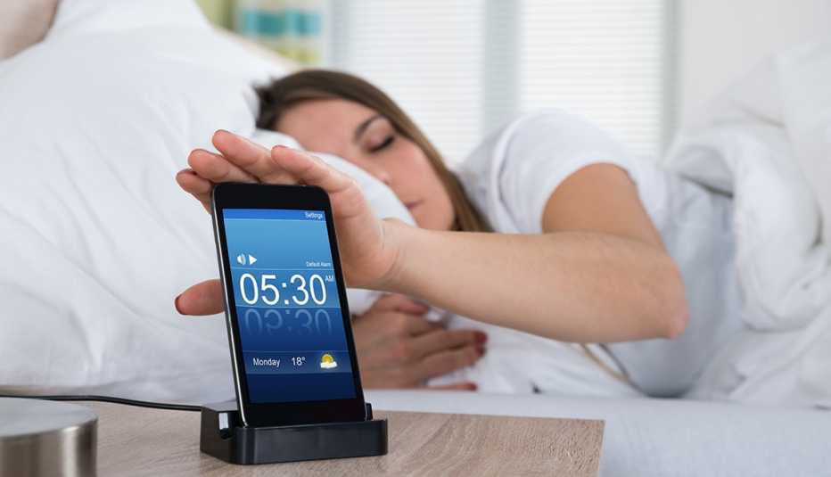 Mujer en una cama con su mano sobre un teléfono móvil cargándose